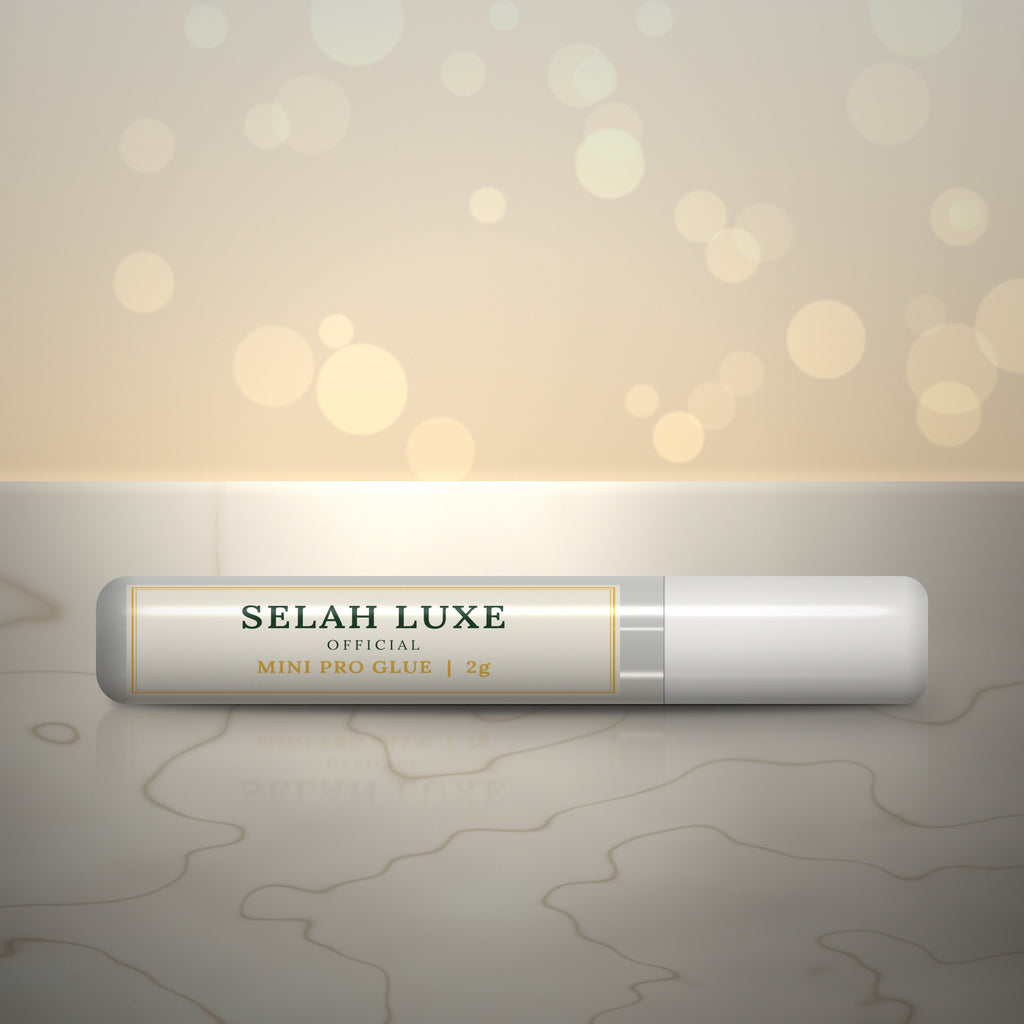 Front of the Selah Luxe Official Mini Pro Glue, 2 g tube, on a cream marble surface